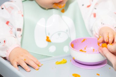 Bebek yüksek sandalyede katı yiyecekler yemeyi öğreniyor.