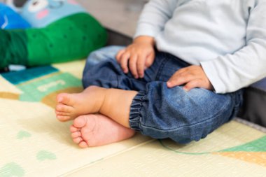 Bebek bebek yumuşak bir oyun hasırının üzerinde oturuyor çıplak ayakla, elleri dizlerinin üstünde