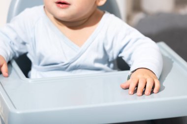 Bebek yüksek bir sandalyede oturuyor, küçük elleriyle tepsiyi inceliyor.