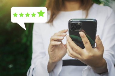 Beş yıldız derecelendirme geribildirim simgesi ile akıllı telefon ekranına kadın eli basarak kapatın ve hizmet sektörü konseptini gözden geçirmek için puan puanı vermek için kademe seviyesine basın.