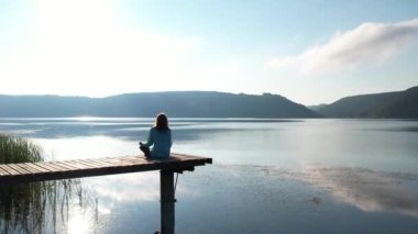 Güzel genç bir kadın ahşap iskelede ruhani yoga pozu veriyor. Gün doğumu