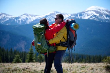 İki yürüyüşçü bir dağ sırtında mola veriyor. Sırt çantalı sportif çift, karlı dağların arka planında duruyorlar..