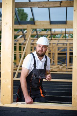 İnşaat işçisi inşaat iskeletinde tahta kirişi mezurayla ölçüyor. Kasklı bir bina, ahşap bina inşaatında çalışıyor..