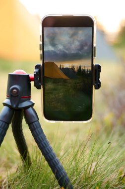 Bir tripodun üzerindeki akıllı telefon, sabahları dağlarda güneşin doğuşunun videosunu çeker. Dağlarda cep telefonu. Yalnız kamp. Cep telefonuyla dağlarda video yakalamak.