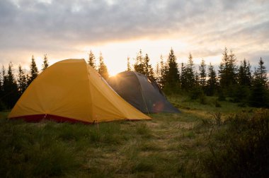 Sabahın köründe tepede iki çadır. Tepeye kurulmuş iki çadır, sabah güneşinin yumuşak ve renkli ışığında yıkanmış. Sabahleyin tepede kamp çadırı.