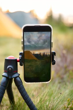 Bir tripodun üzerindeki akıllı telefon, sabahları dağlarda güneşin doğuşunun videosunu çeker. Dağlarda cep telefonu. Yalnız kamp. Cep telefonuyla dağlarda video yakalamak.