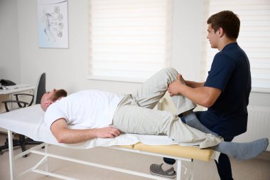 Modern tıp kliniğindeki rehabilitasyon seansında hastanın diz eklemlerini muayene eden fizyoterapist. Yaraları için ortopedik tedavi ve fizik tedavi gören bir adam..