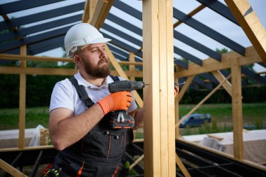 Ahşap çerçeve inşa ederken elektrikli tornavida kullanan inşaat işçisi. Koruyucu kasklı adam, eldiven. İnşaat, marangozluk, mühendislik ve inşaat süreci kavramı.