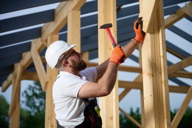 İnşaat işçisi inşaat alanındaki tahta kirişleri korumak için çekiç kullanıyor. İnşaat, marangozluk, inşaat süreci, işçilik ve el işçiliği kavramı.