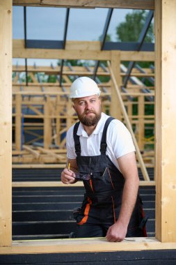 İnşaat işçisi inşaat iskeletinde tahta kirişi mezurayla ölçüyor. Kasklı bir bina, ahşap bina inşaatında çalışıyor..
