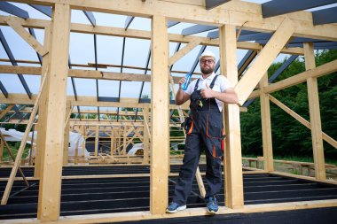 İnşaat işçisi ahşap ev iskeleti şantiyesinde mola verip su içiyor. İnşaatçı kaskı ve su şişesiyle dinleniyor..