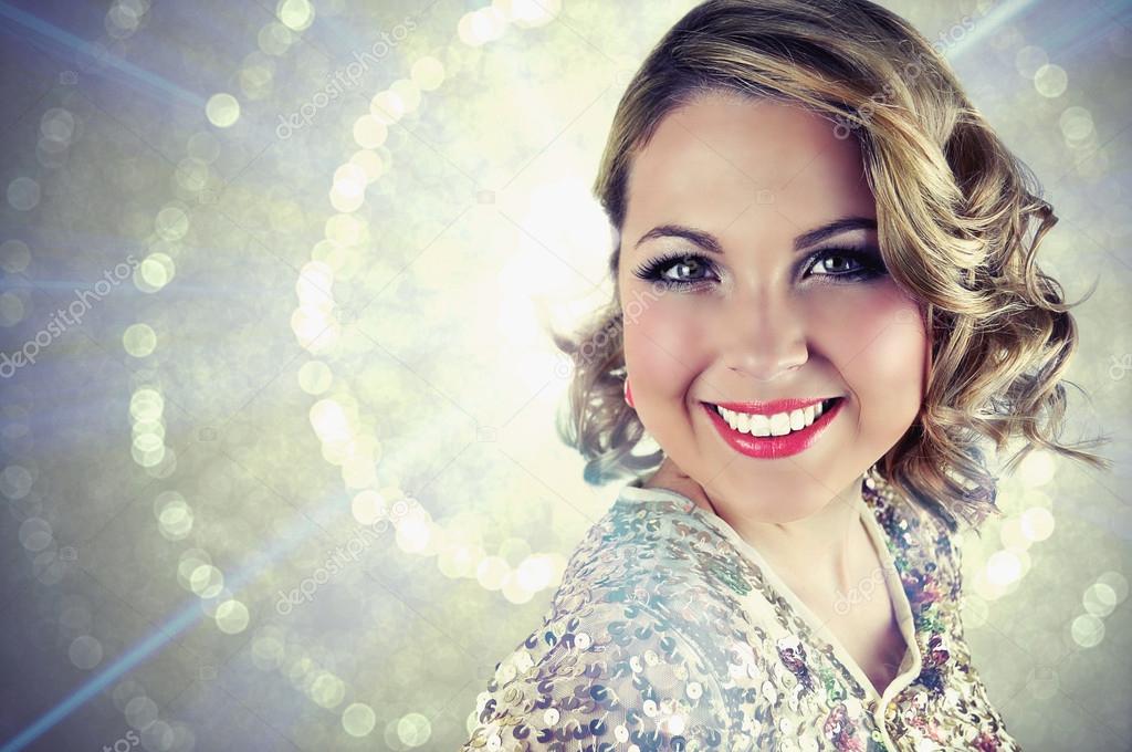 Beautiful smiling blonde woman with curly shoulder length hair wearing evening make-up and a golden sparkly sequin bolero.