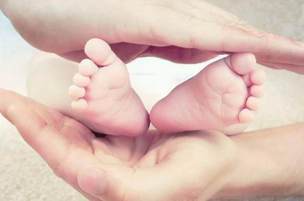 Pequenos pés de bebê cercados por pais mãos fortes . Fotos De Bancos De Imagens Sem Royalties