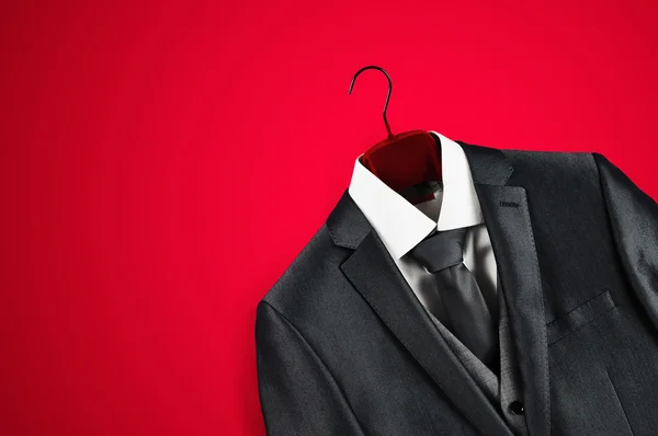 Mens terno cinza escuro no cabide de roupas no fundo vermelho . Fotos De Bancos De Imagens Sem Royalties