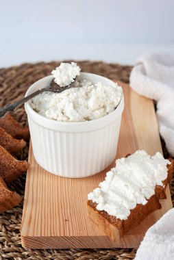 Beyaz seramik kasede taze ricotta peyniri ve ahşap kesim tahtasında çavdar sandviçi.