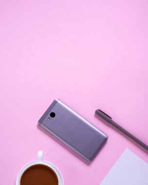 Akıllı telefonlu en az masa başı masa, bir fincan kahve, kağıt ve pembe arka planda kalem. Üst manzara, düz uzanma.