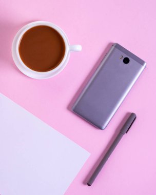Akıllı telefonlu en az masa başı masa, bir fincan kahve, kağıt ve pembe arka planda kalem. Üst manzara, düz uzanma.