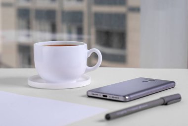 Ofis masası, akıllı telefon, bir fincan kahve, kağıt ve kalem pencerenin karşısında.