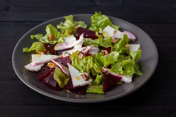Fırında pancar salatası, yumuşak peynir ve siyah tabakta fındık.