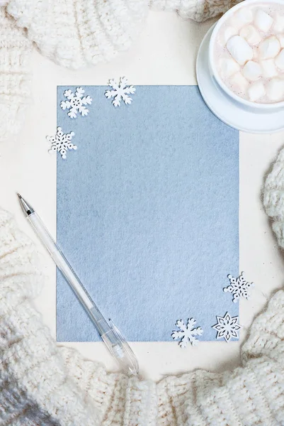Küçük kar tanelerinden beyaz çerçeveli gri gümüş kağıt, bir fincan çikolata, kalem ve örgü atkı. Kış ya da Noel konsepti, düz konum, üst görünüm, kopyalama alanı