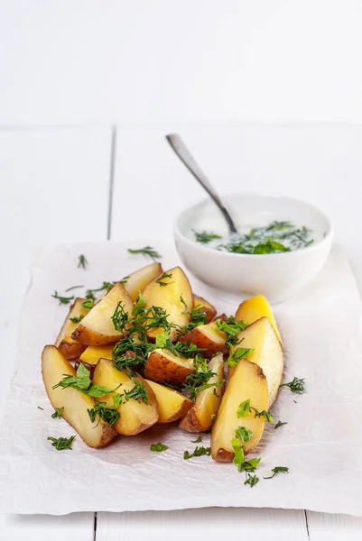 Beyaz ahşap arka planda dereotlu ve maydanozlu fırında patates dilimleri.
