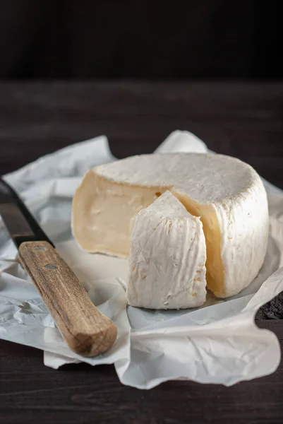 Doğal koyu ahşap arka planda kremalı Camembert peyniri, beyaz kağıttan yeni açılmış, ayrı bir parça ile.