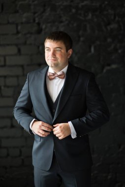 Siyah arka planda takım elbisenin düğmelerini ilikleyen bir adam.