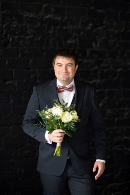 Takım elbiseli damat düğün buketi taşıyor.