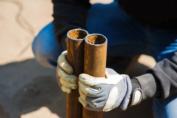 A worker holds in his hands two pieces of a metal pipe cut off