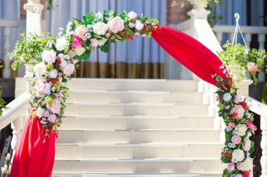 Yapay çiçekler ve kırmızı kumaştan yapılmış düğün kemeri.