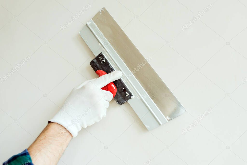 Worker hand with spatula on white wall