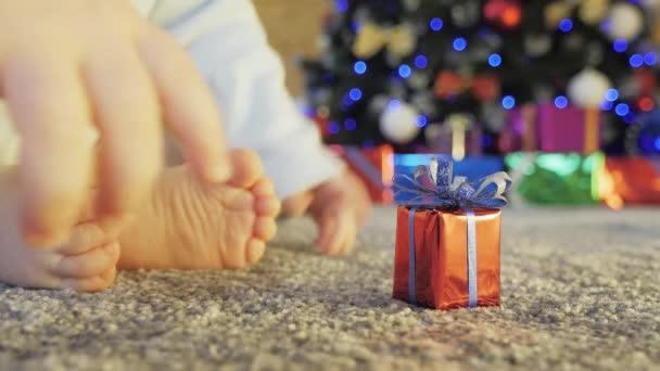 Barnet plockar upp en present nära dekorerad julgran — Stockvideo