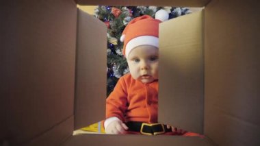Çocuk süslenmiş bir Noel ağacının yanında bir Noel hediyesi açar.