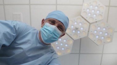 Cerrahi şapkalı ve koruyucu maskeli doktor hastaya bakar.
