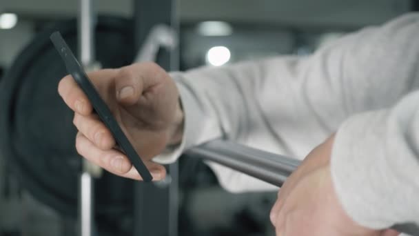 Culturista mira el teléfono inteligente en el gimnasio — Vídeo de stock