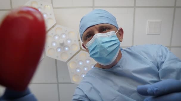 Cirurgião com coração vermelho perto da mesa de cirurgia — Vídeo de Stock