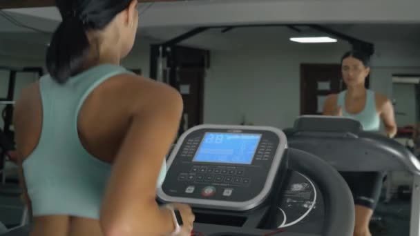 Mujer atlética se ejecuta en una máquina de cinta de correr en un gimnasio. — Vídeos de Stock