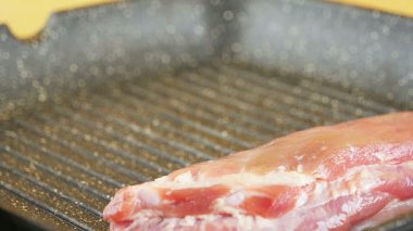 Domuz filetosu kızgın bir ızgara tavasına konmuş, yakılmaya hazır. Pişirme sıcaklıkları ve sıvılığı et pişerken vurgulanıyor.