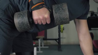Spor salonunda kaslarını şişiren kaslı ve atletik bir adam. Yakın planda el kamerasıyla çekilmiş.