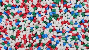 Kırmızı, beyaz, yeşil ve mavi kapsüller düz bir yüzeye dağılmıştır. Düzenleme farklı şekil ve boyutlarda renkli haplar gösteriyor..