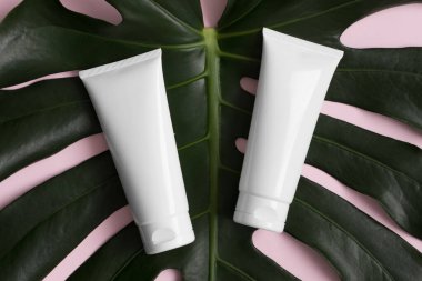 Pembe arka planda canavar yaprağı olan beyaz krema tüplerinin üst görüntüsü..