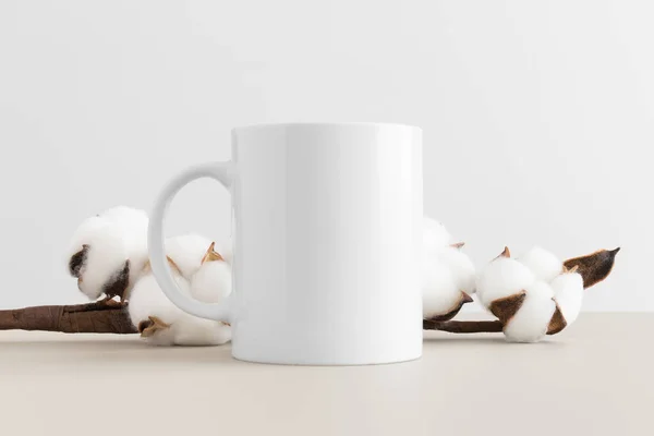 ベージュのテーブルの上に綿の枝と白いマグカップのモックアップ — ストック写真