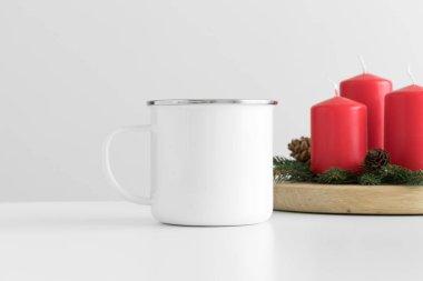 Masasında mumlar olan Enamel beyaz kupa. Noel süslemesi