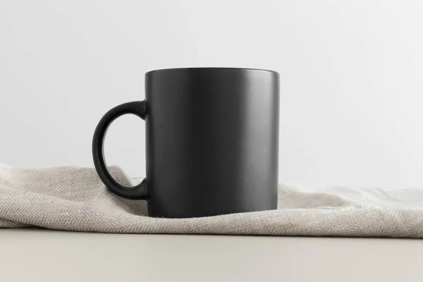 Black mug mockup with a table cloth on a beige table.