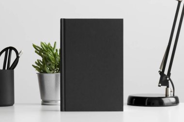Beyaz bir masa üzerinde sulu bir bitki ve çalışma alanı aksesuarları olan siyah kitap modeli..