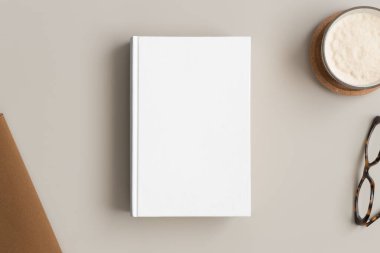 Bej bir masa üzerinde kahve ve çalışma alanı aksesuarları olan beyaz kitap modeli..