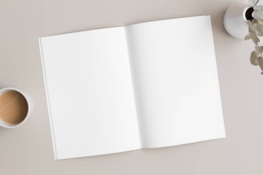 Açık dergi modeli, bir fincan kahve ve bej masa üzerinde okaliptüs..