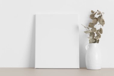 Bej masasında okaliptüs olan beyaz tuval..