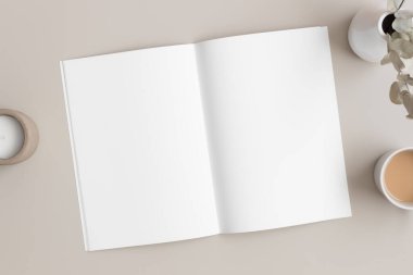 Bej masasında bir kitap, mum ve okaliptüs olan açık dergi modeli..