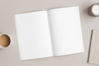 Açık dergi modeli, bir fincan kahve, mum ve bej masanın üzerinde bir defter..